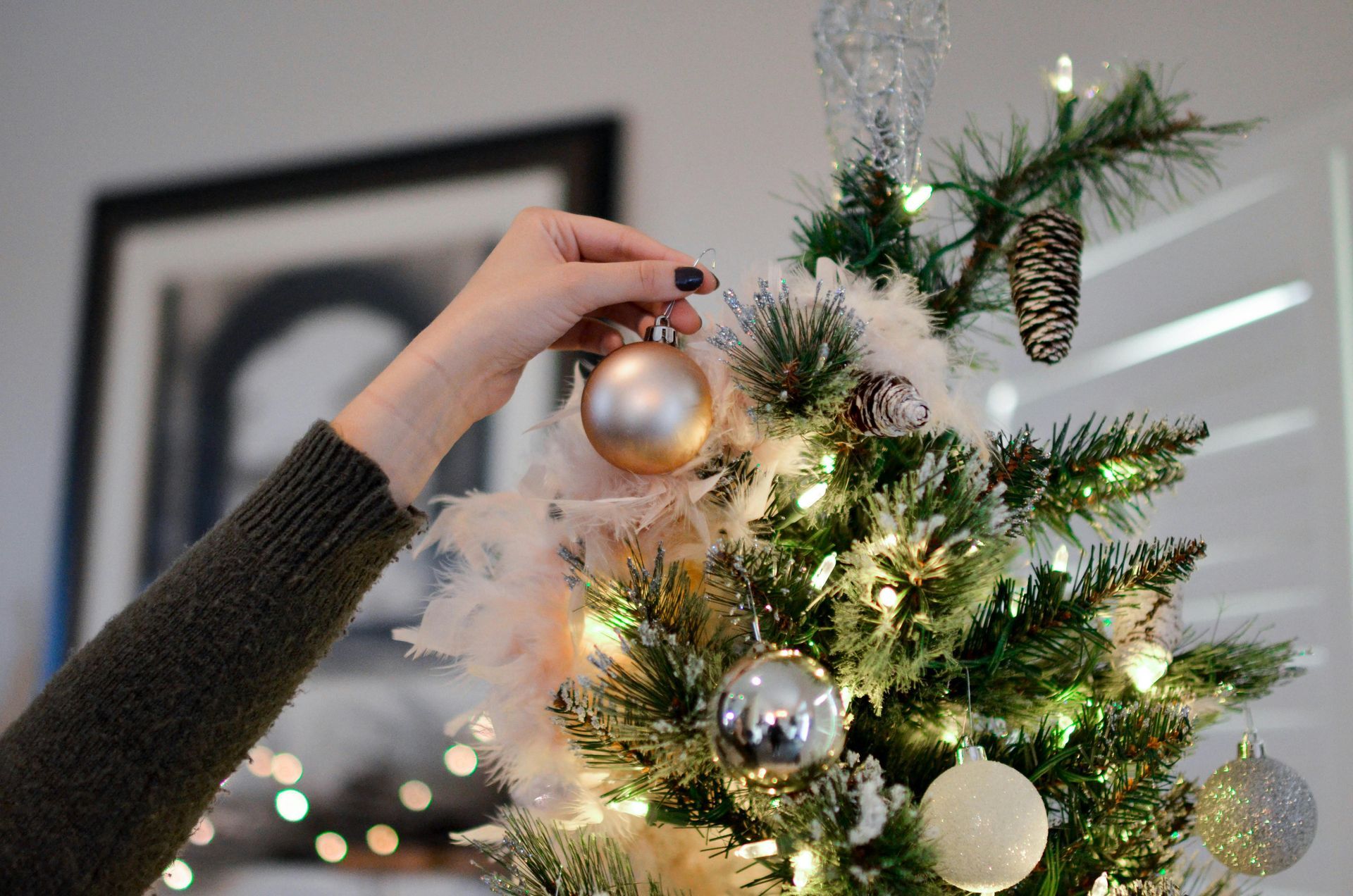 Person decorates a Christmas tree, hanging a gold ornament.