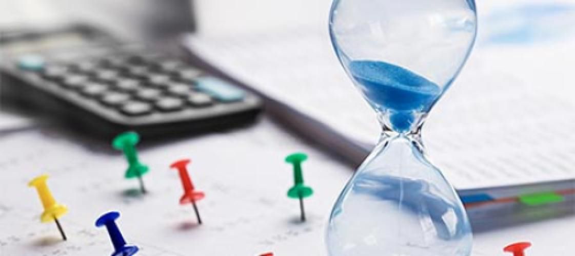 A hourglass is sitting on top of a calendar next to a calculator.