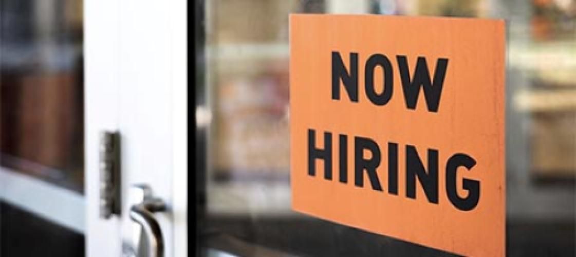 A now hiring sign is on a glass door.
