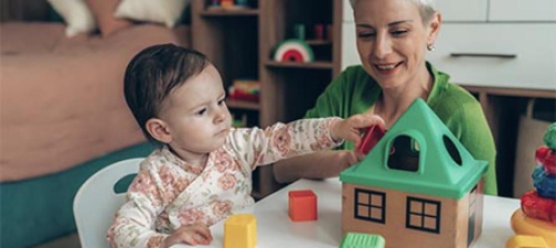 A woman and a baby are playing with toys at a table.