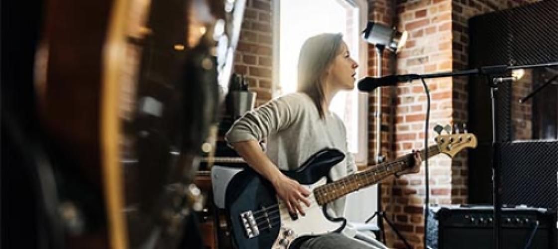 A woman is playing a guitar in front of a microphone in a recording studio.