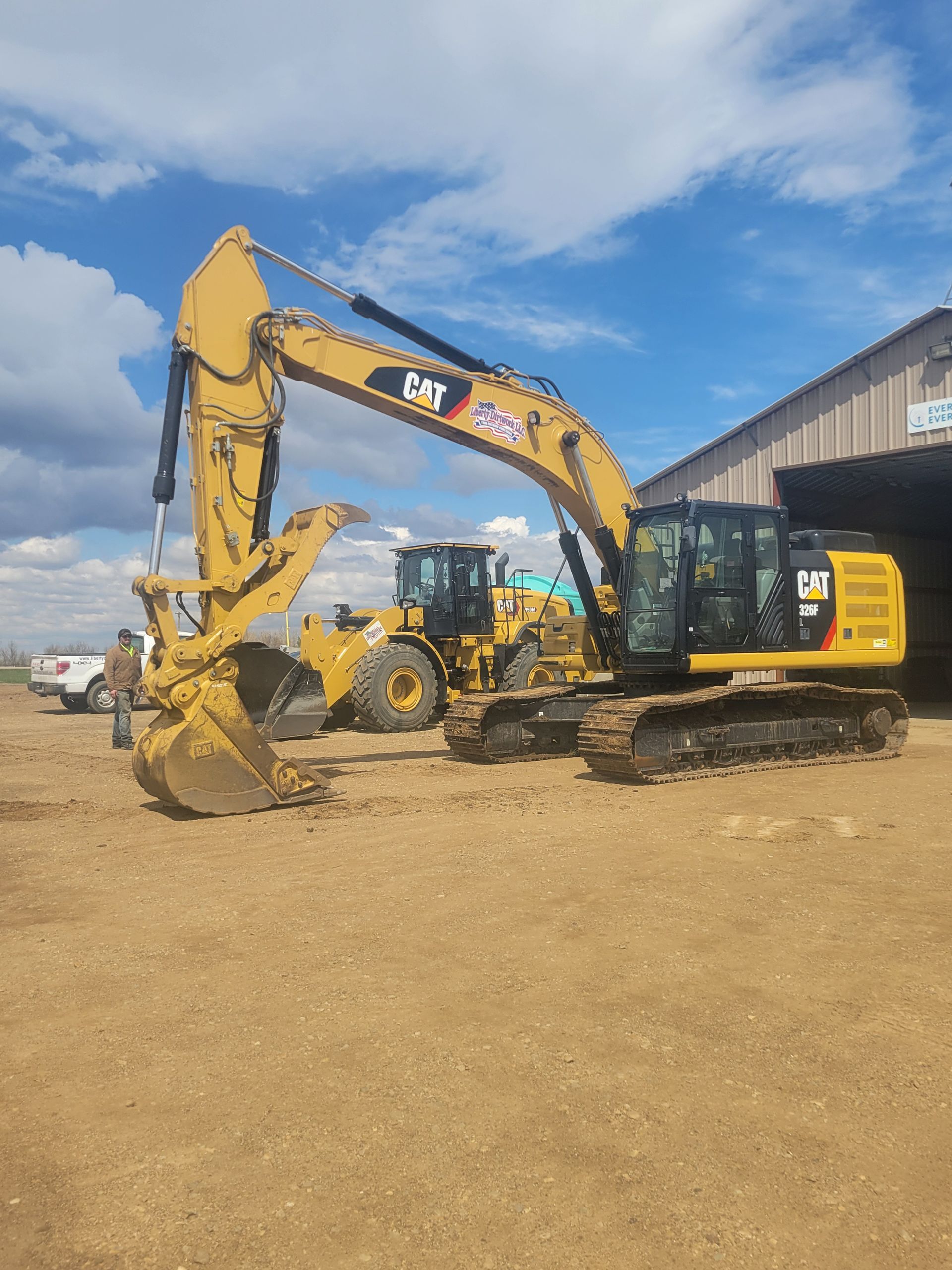 Yellow Caterpillar excavator and other construction equipment outside a building under a cloudy sky.