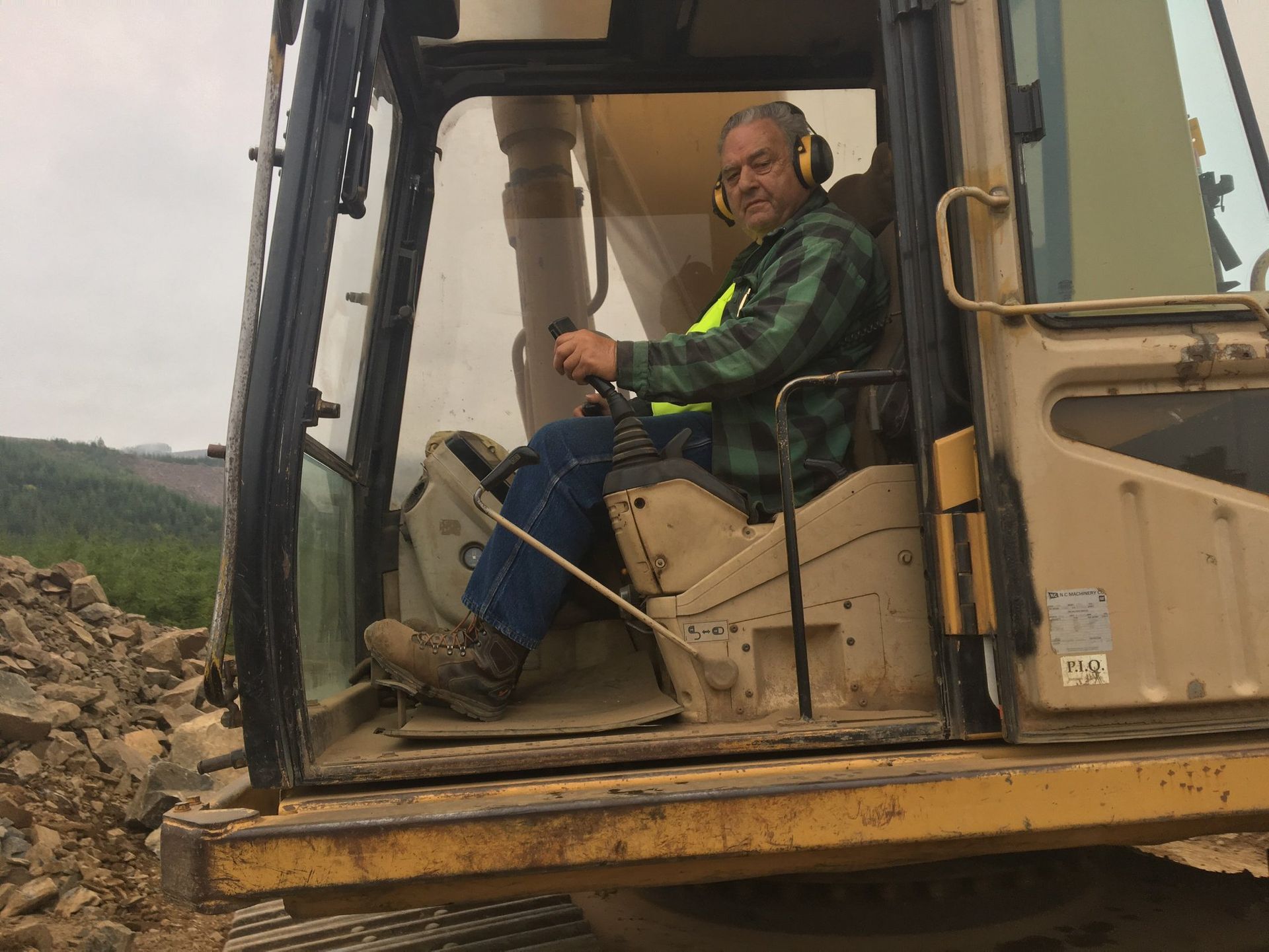 Man sitting in the cab of a beige excavator at a rocky construction site