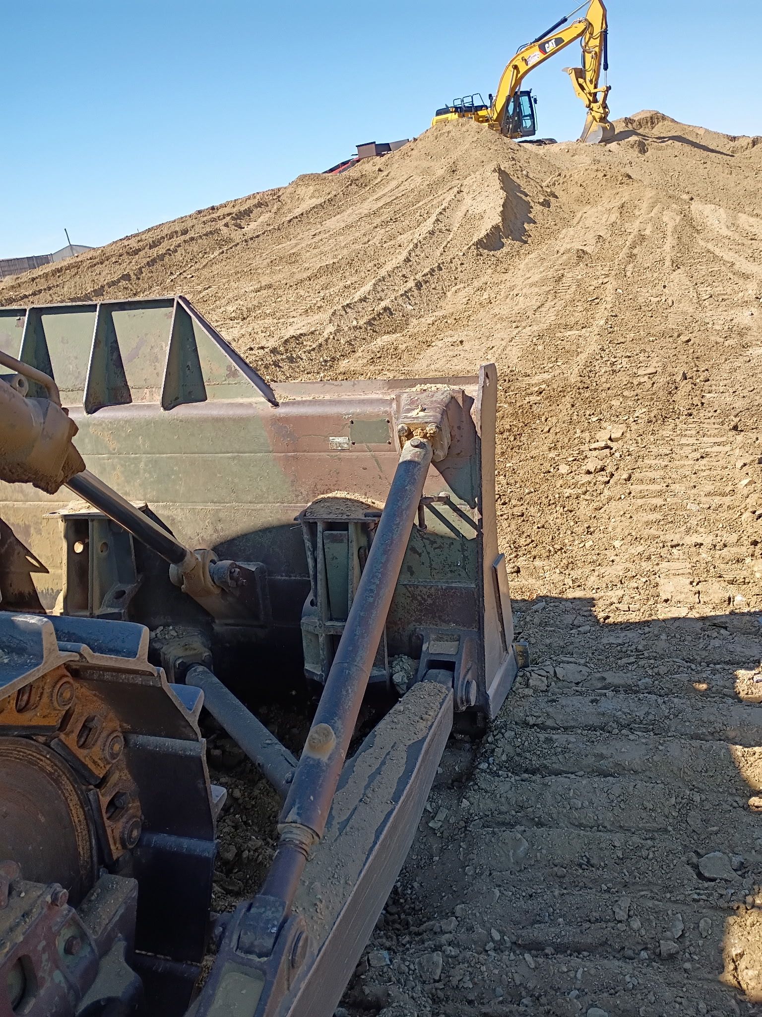 Bulldozer pushing sand, excavator on top of a large pile of sand, clear sky.
