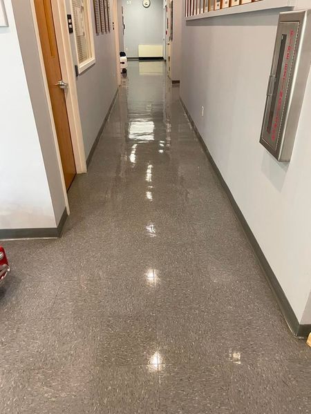 Long hallway with a shiny, gray floor, gray walls, and a wooden door.