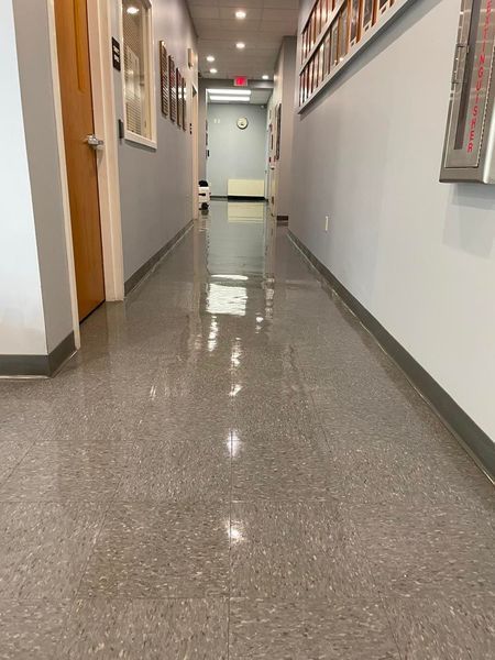 Long hallway with shiny gray flooring and light blue walls, featuring a wooden door and a few framed items.