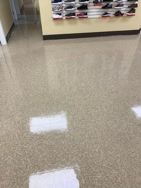 Tan speckled flooring in a store. Shoes displayed on a wall in the background.