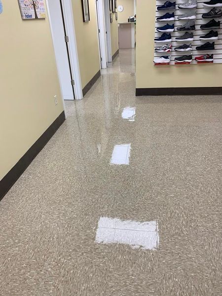 Hallway with cream-colored speckled flooring, with three rectangular, white patches on the floor. Shoe display on the right.