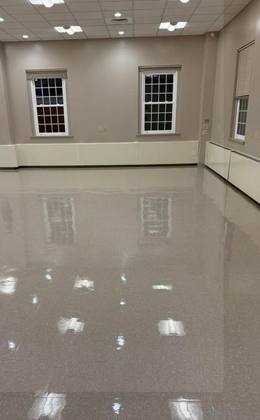 Empty, bright room with reflective floor and three windows, off-white walls, and ceiling lights.