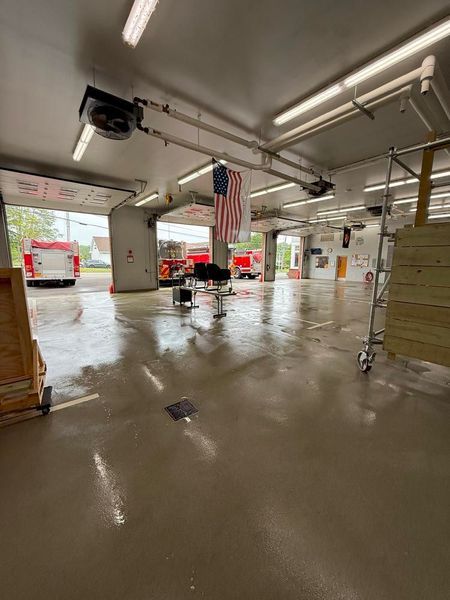 Empty fire station bay; two fire trucks visible. American flag hangs from ceiling.