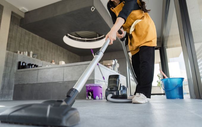 Woman in yellow apron vacuums a gray floor in a modern kitchen.