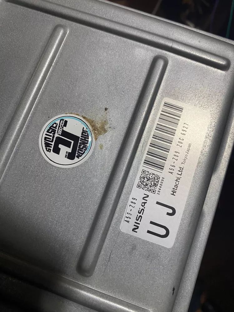 A close up of a nissan engine control module with a sticker on it.