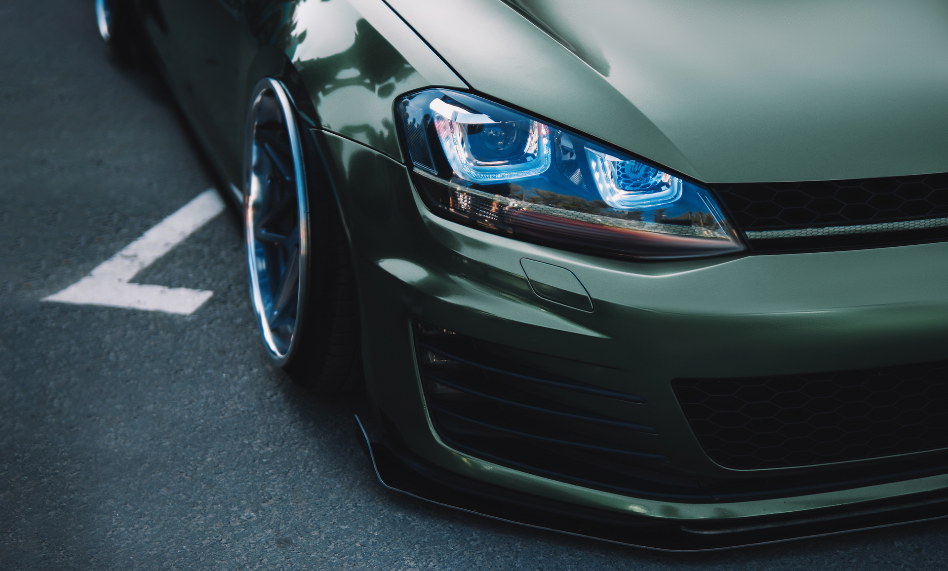 A green car with blue headlights is parked in a parking lot.