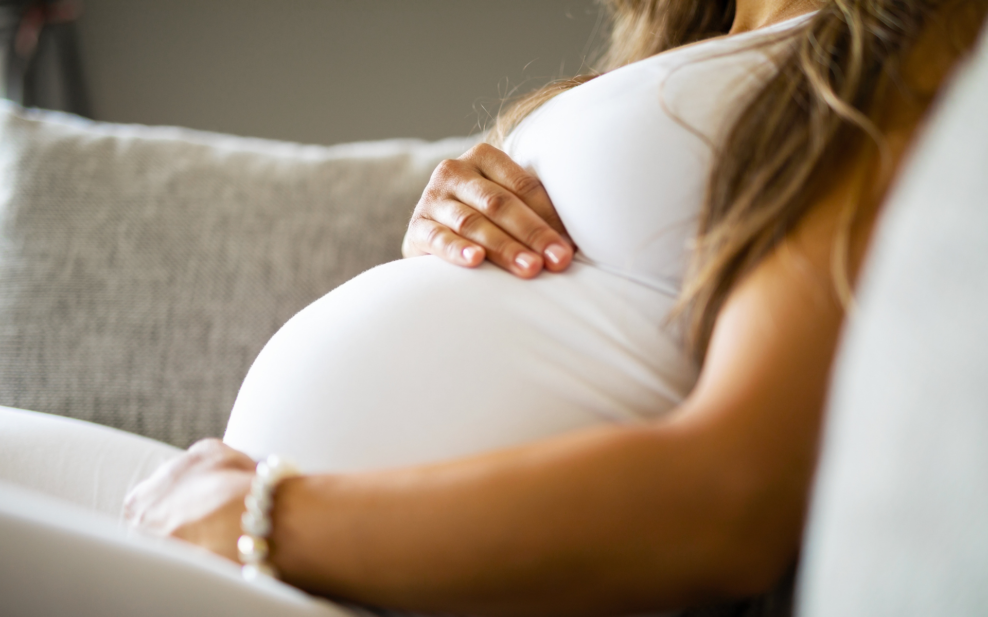 A pregnant woman sitting on the couch holding her stomach