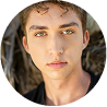 Young man with light skin, green eyes, and curly brown hair, looking directly at the camera.