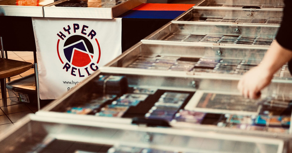 Person browsing cards in glass display cases at a Hyper Relic booth.