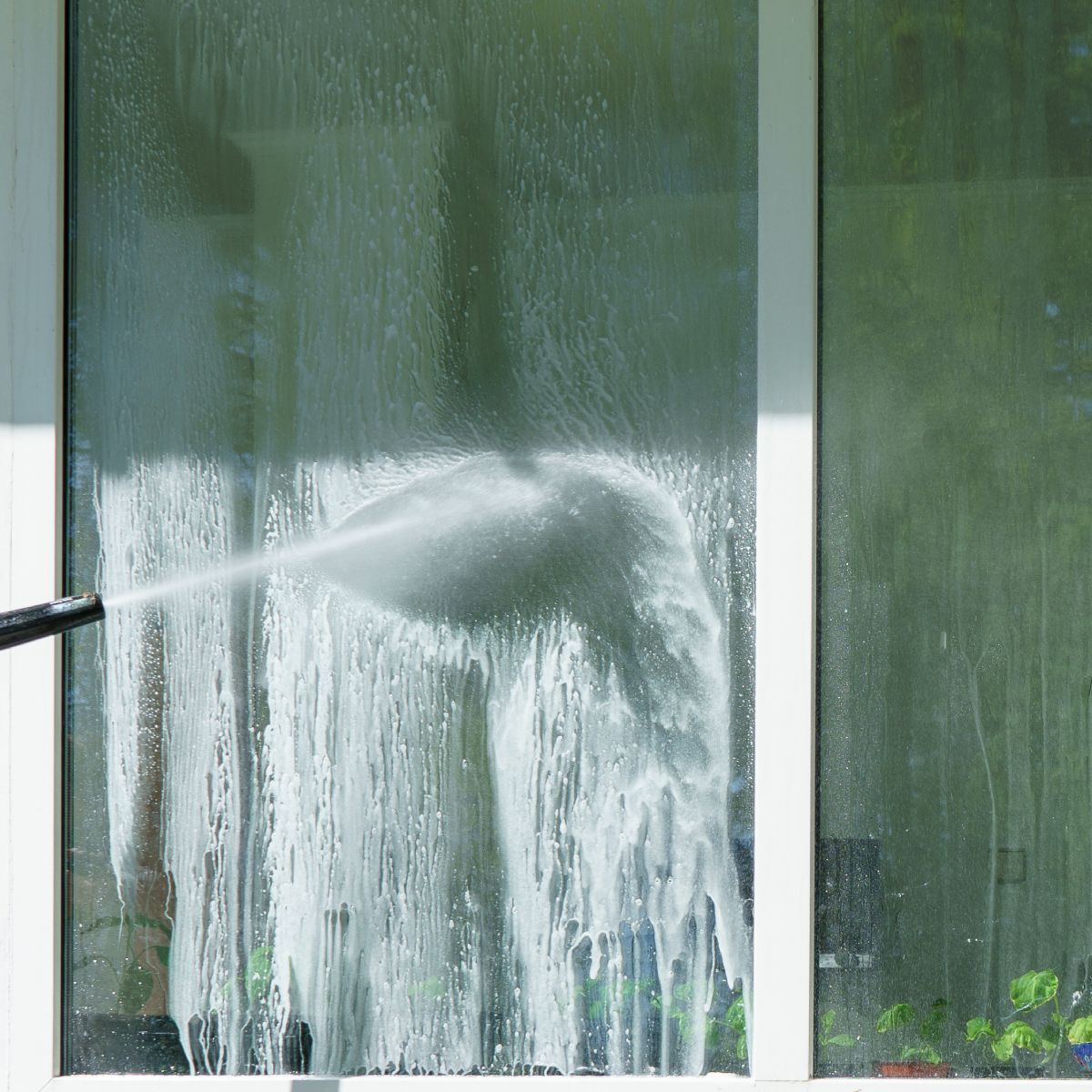 A person is cleaning a window with a high pressure washer.