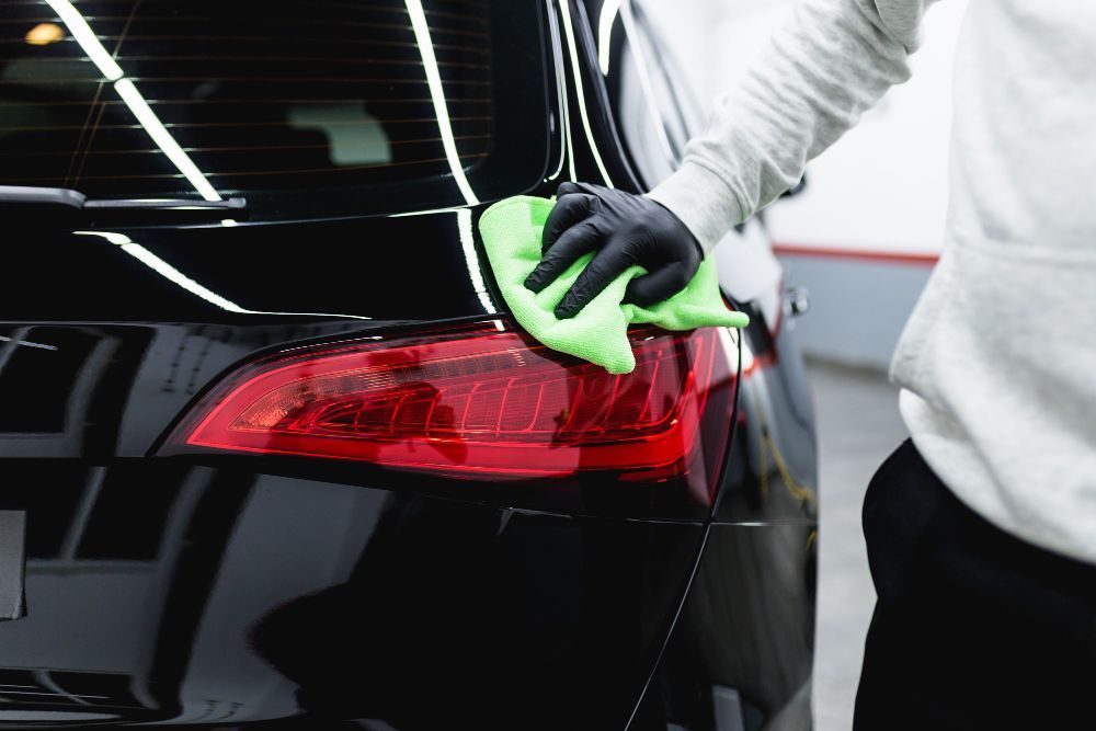 A person is cleaning the tail light of a car with a green cloth.