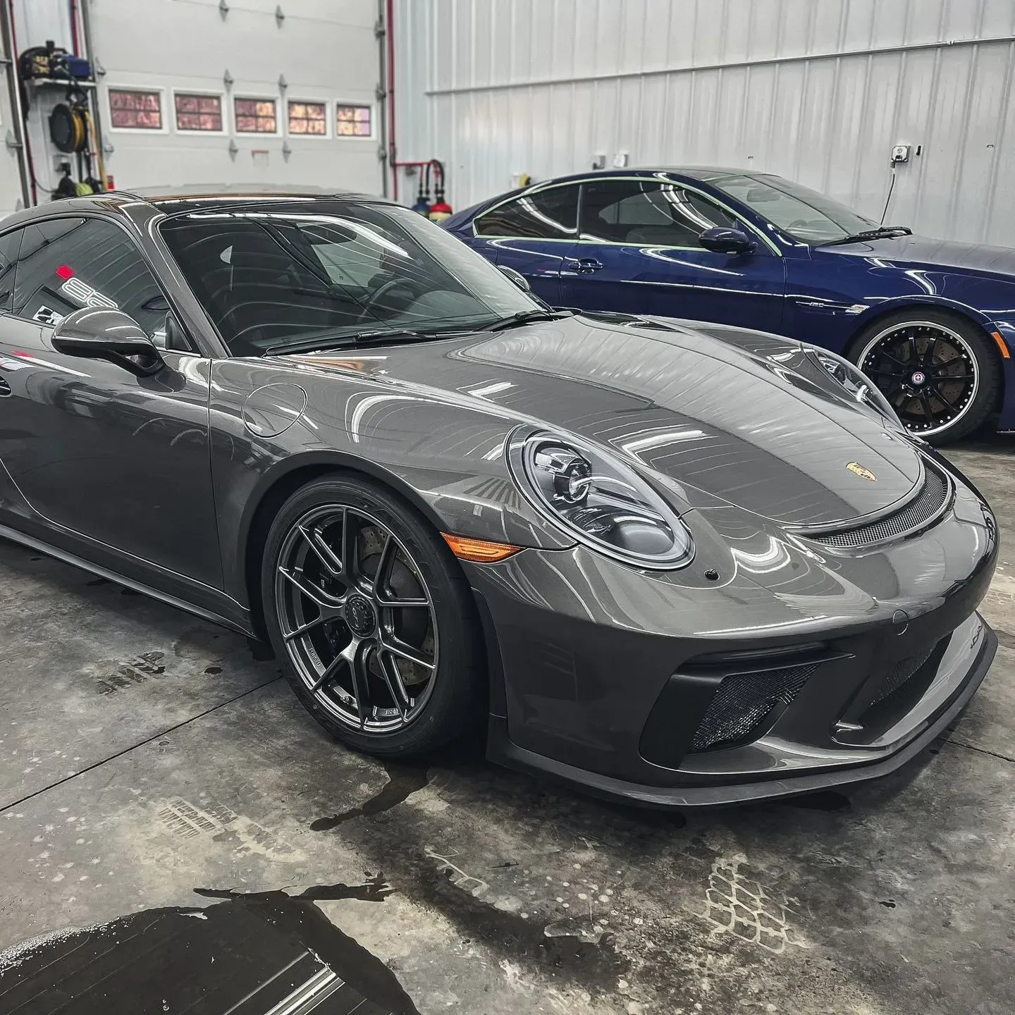 A gray sports car is parked next to a blue sports car in a garage.