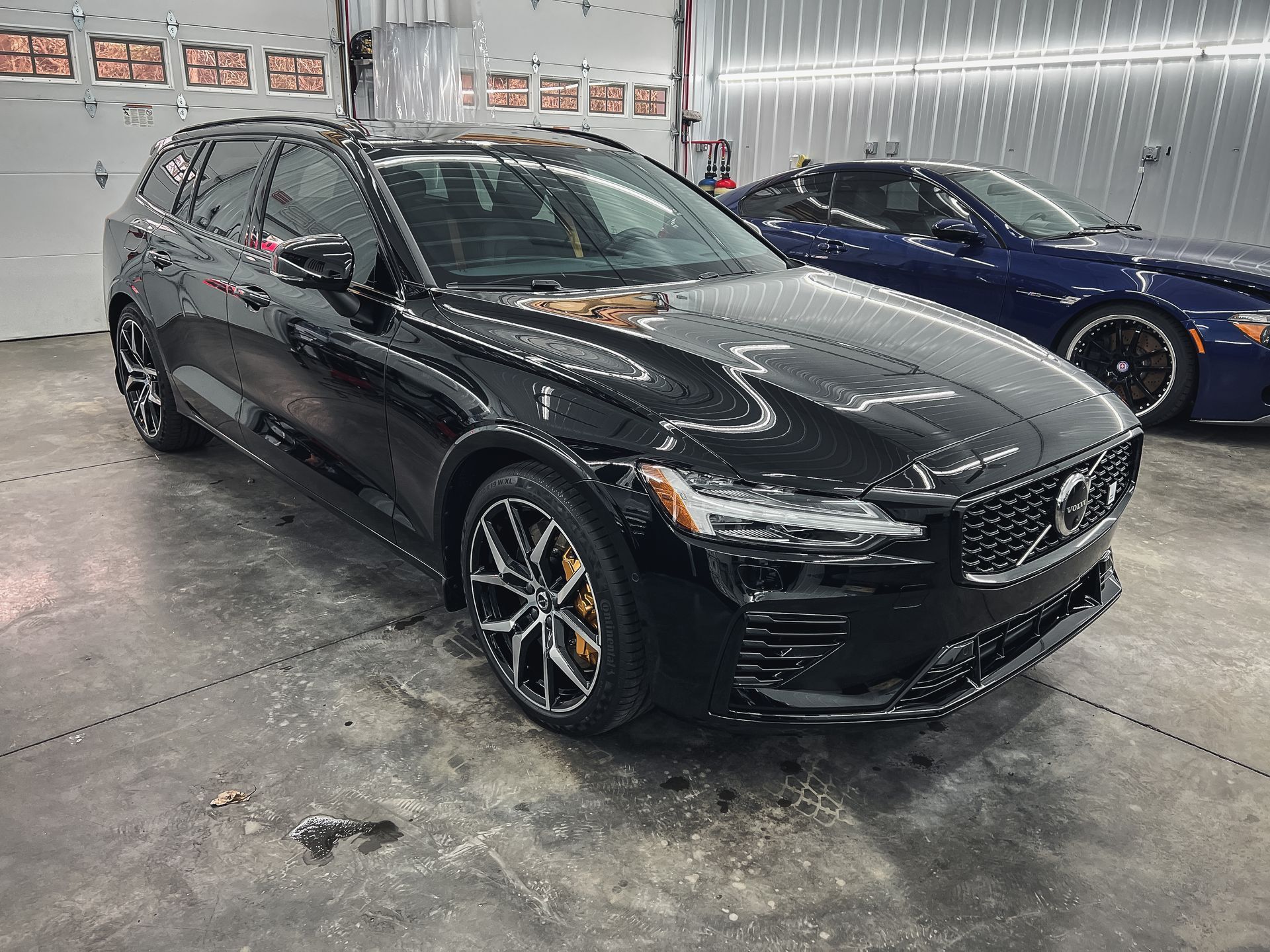 A black volvo s60 is parked in a garage next to a blue sports car.
