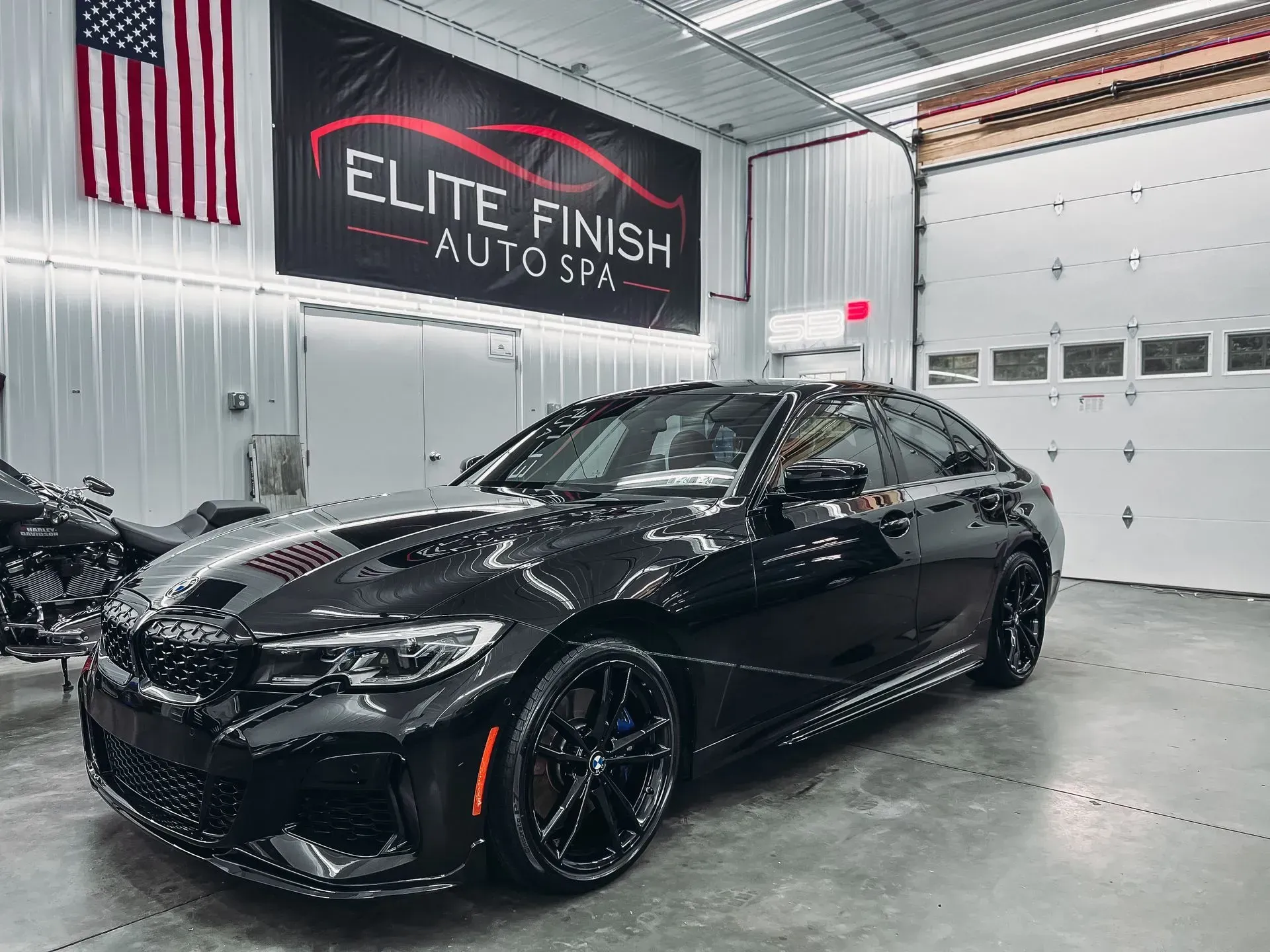 A black car is parked in a garage next to an american flag.