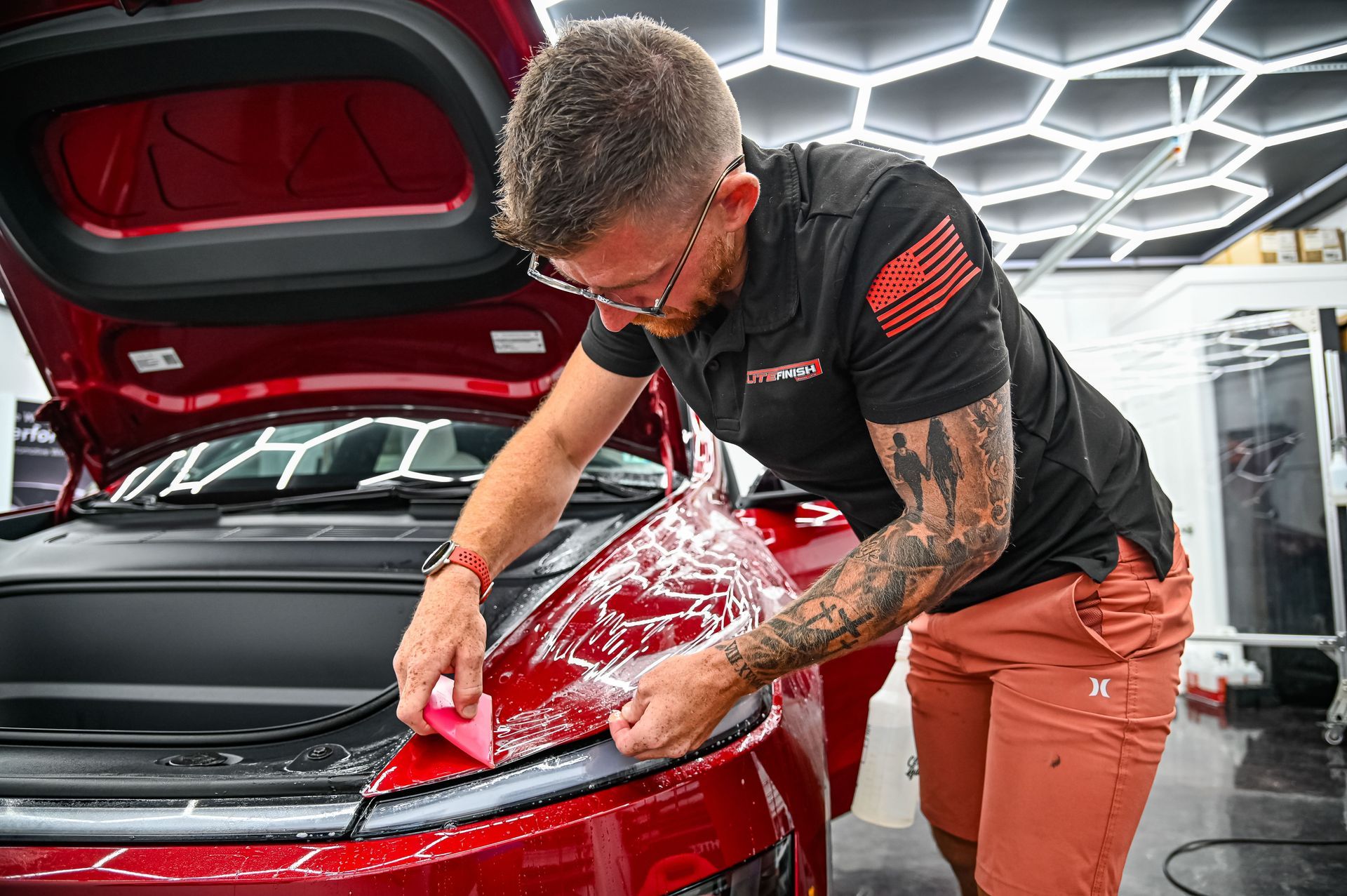 Detailer installing PPF on a red sports car’s front hood in a bright garage.