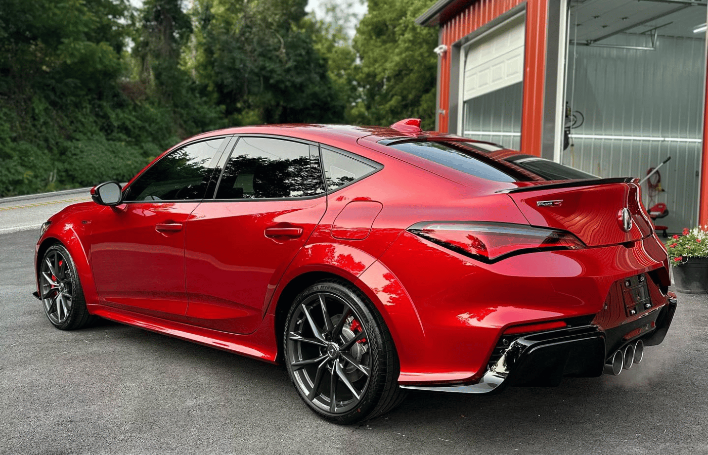 Red sports coupe parked outside a garage, shown from the rear three-quarter angle.