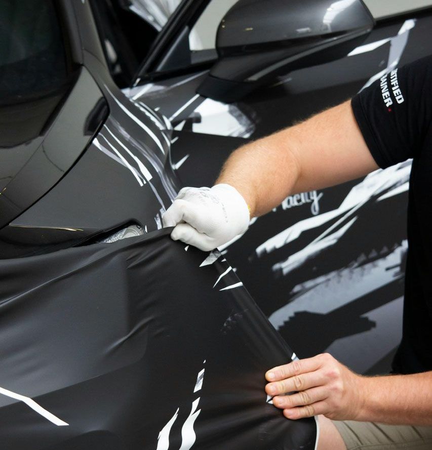 A man is wrapping a black car with a black shirt that says united states marines