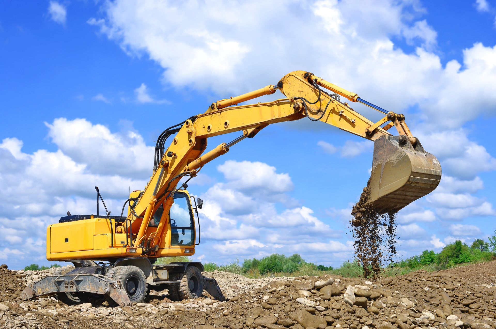 Un escavatore giallo scarica terra in un cantiere edile sotto un cielo azzurro.