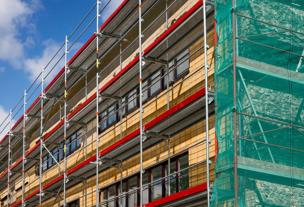 Impalcature sul lato di un edificio in costruzione, con reti di sicurezza e cielo azzurro.