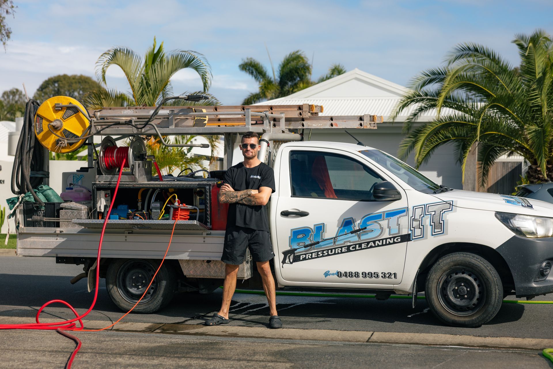 Man standing next to a white service truck with company logo, equipment, and a ladder, on a residential street — Blast It Pressure Cleaning - Gold Coast In Gold Coast, QLD