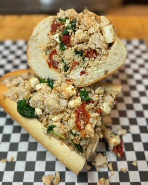 A sandwich stuffed with eggs, tomatoes, and greens on checkered paper.