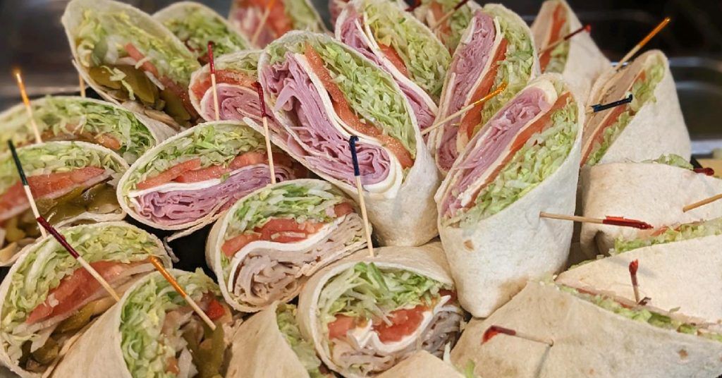 Assorted sandwich wraps filled with lettuce, ham, and tomato, arranged in a close-up display.