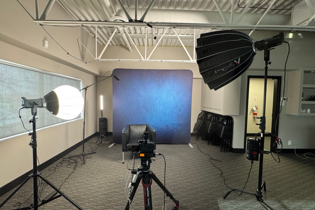 Photo studio with blue backdrop, lighting umbrellas, and camera on tripod ready for a shoot.