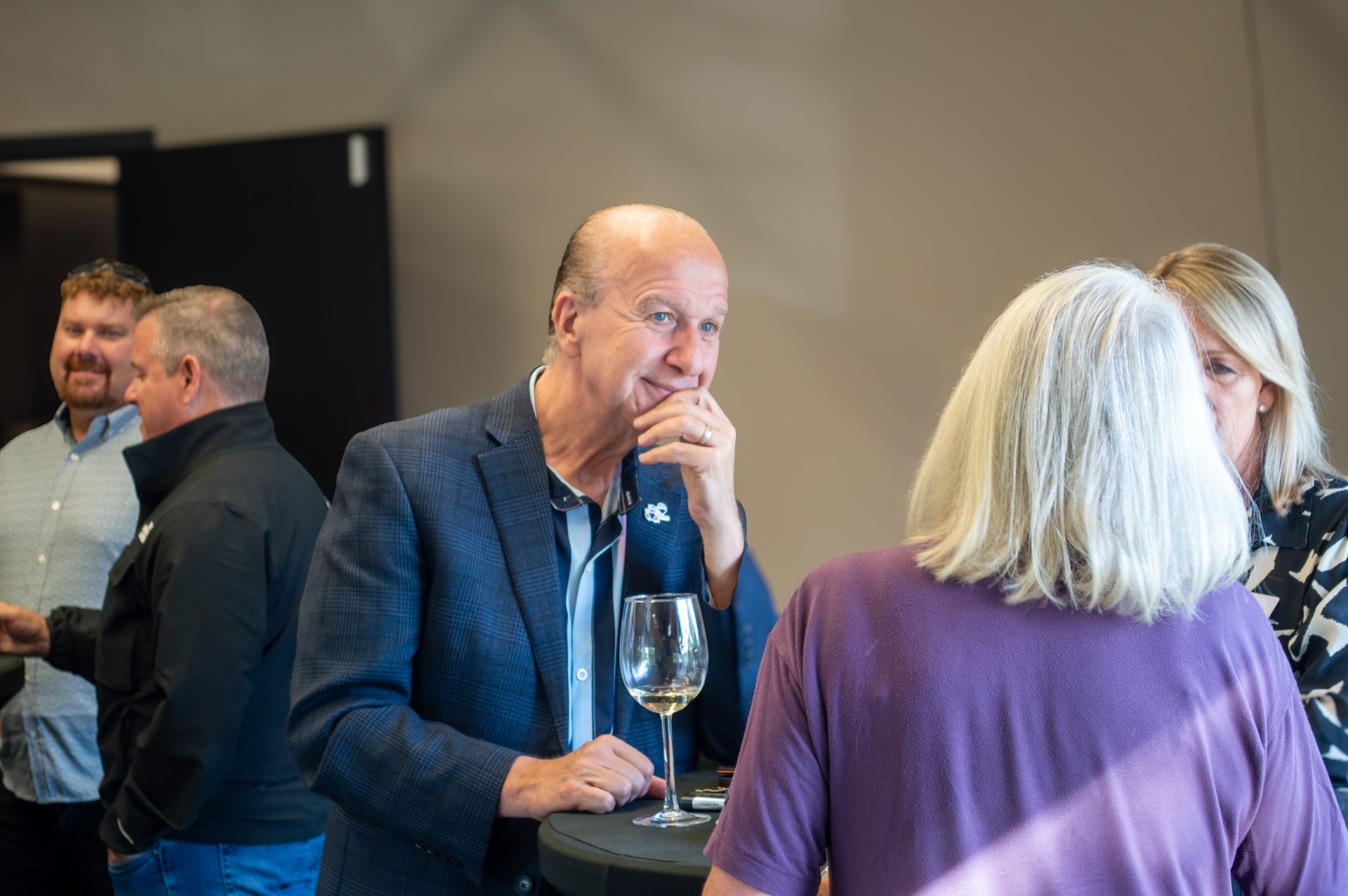 People chatting at a conference reception, holding wine glasses near a doorway.