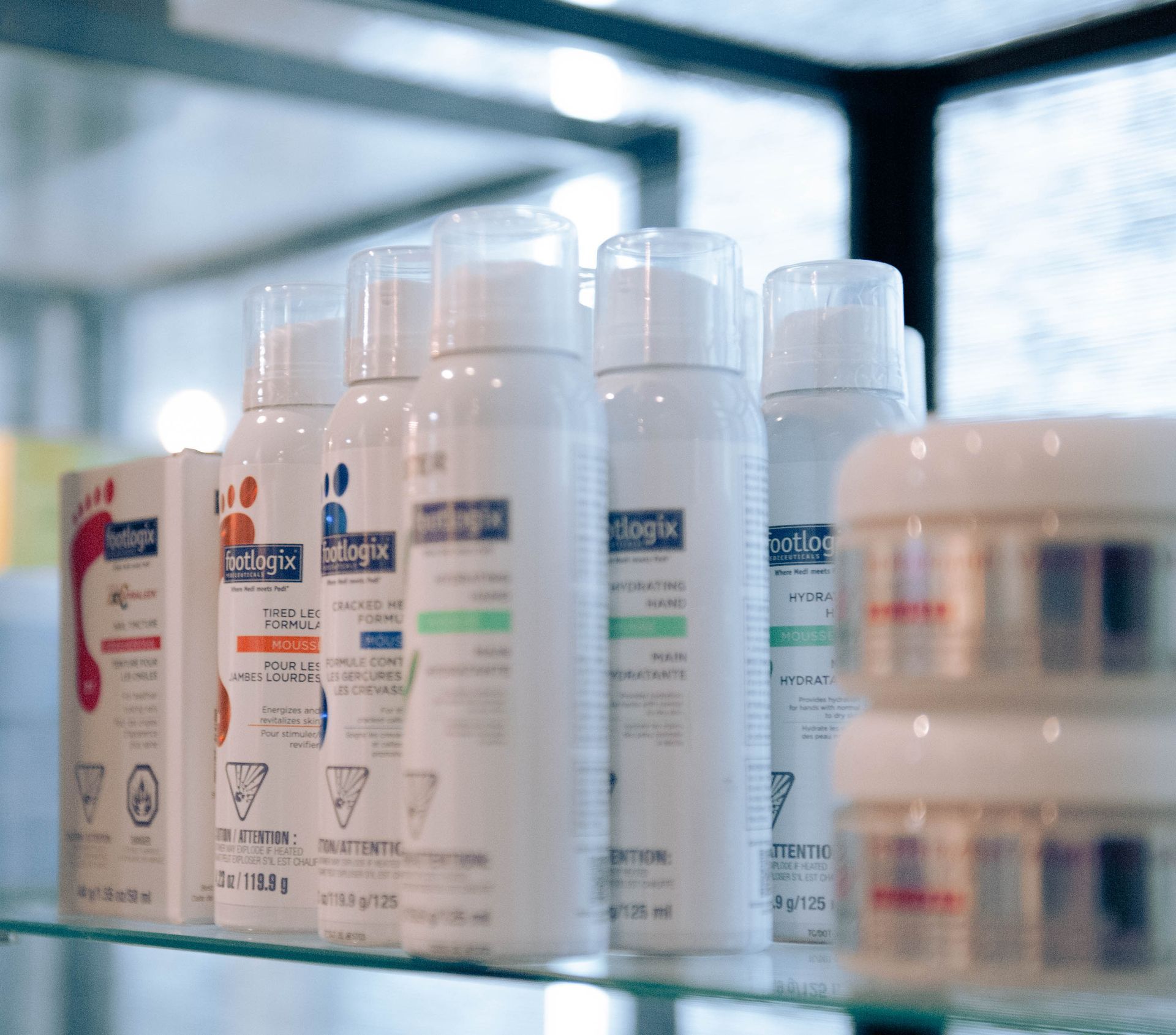 White cosmetic bottles and jars lined up on a glass shelf in a bright store aisle