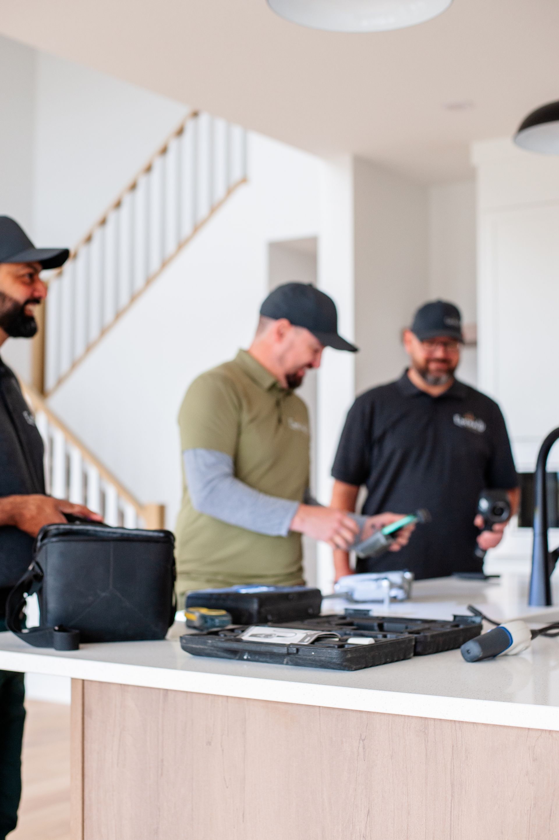 Three men examining equipment on a kitchen island in a bright modern home