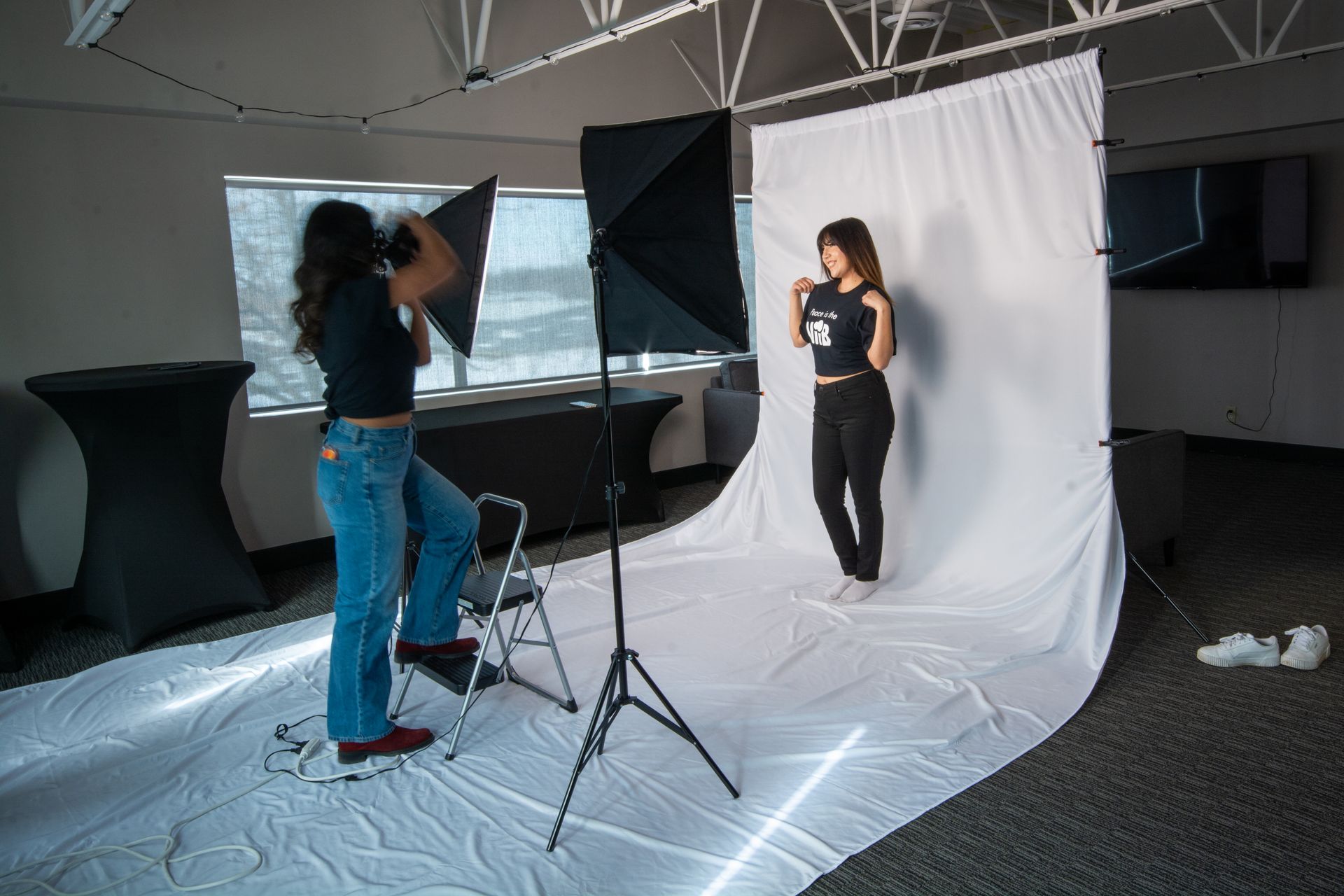 Photographer taking a portrait of a woman against a white backdrop in a studio setup