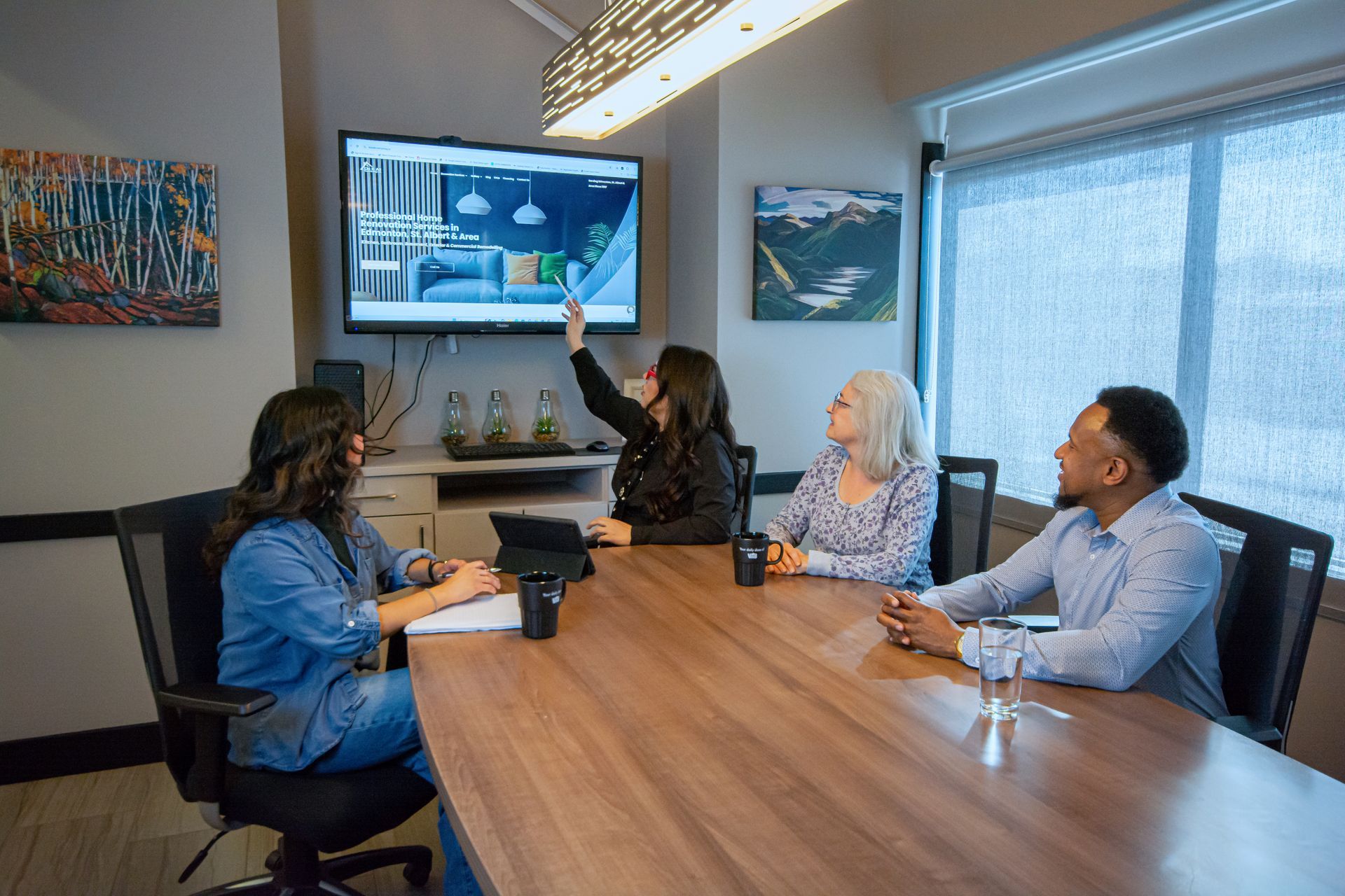 Four people in a conference room discuss a presentation on a wall screen.