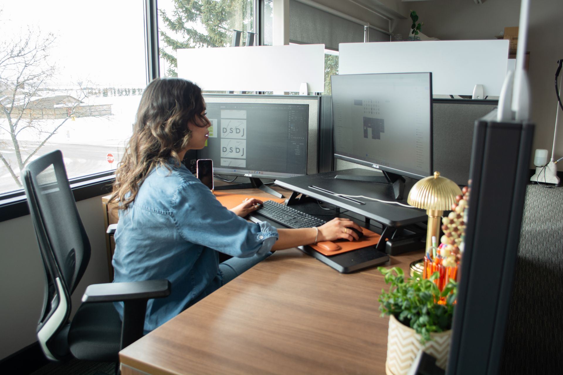 Woman working at a desk with dual monitors in a bright office workspace