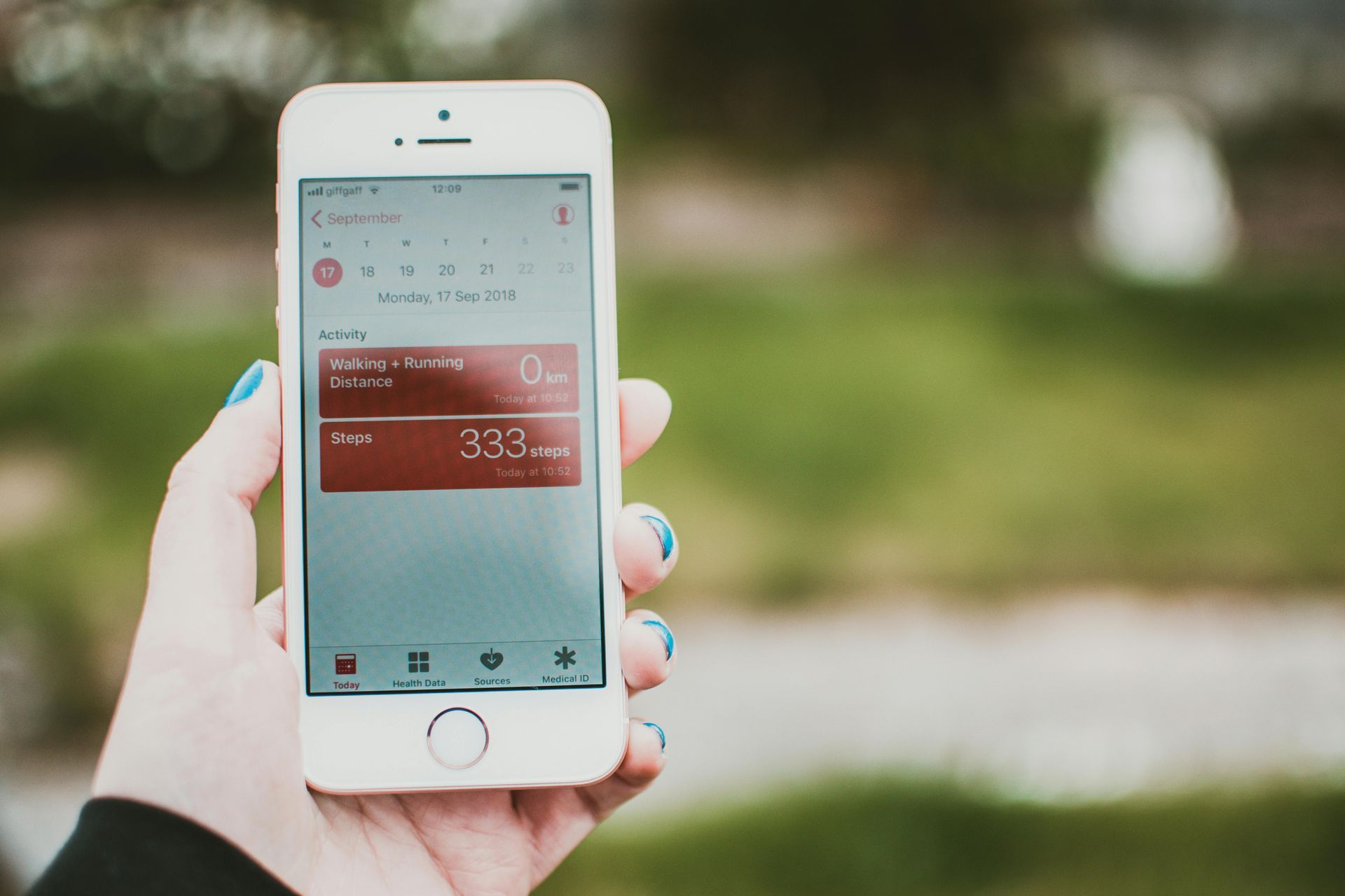 Hand holding a white smartphone showing a weather app outdoors on a blurred green background