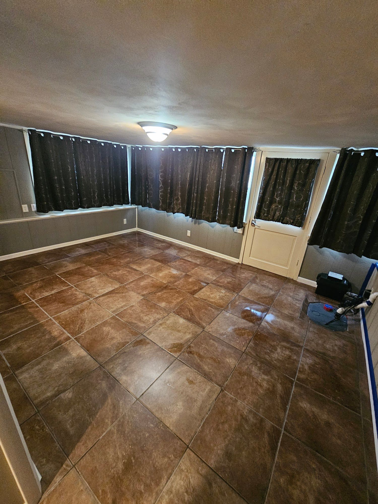 A living room with tile floors , curtains , and a door.