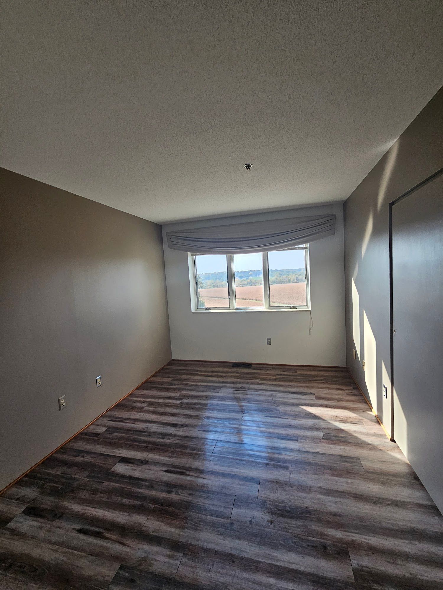 An empty living room with hardwood floors and a large window.