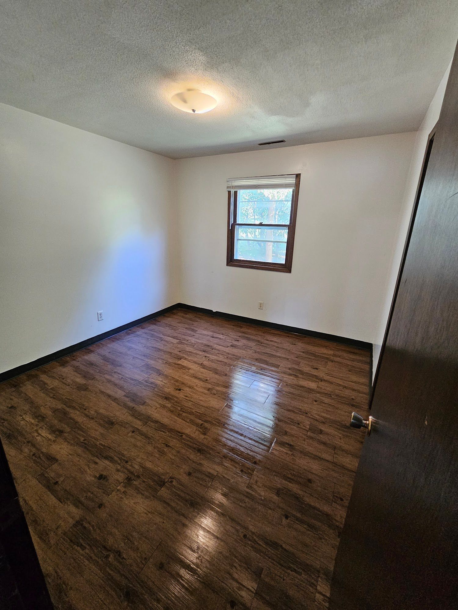 An empty bedroom with hardwood floors and a window.