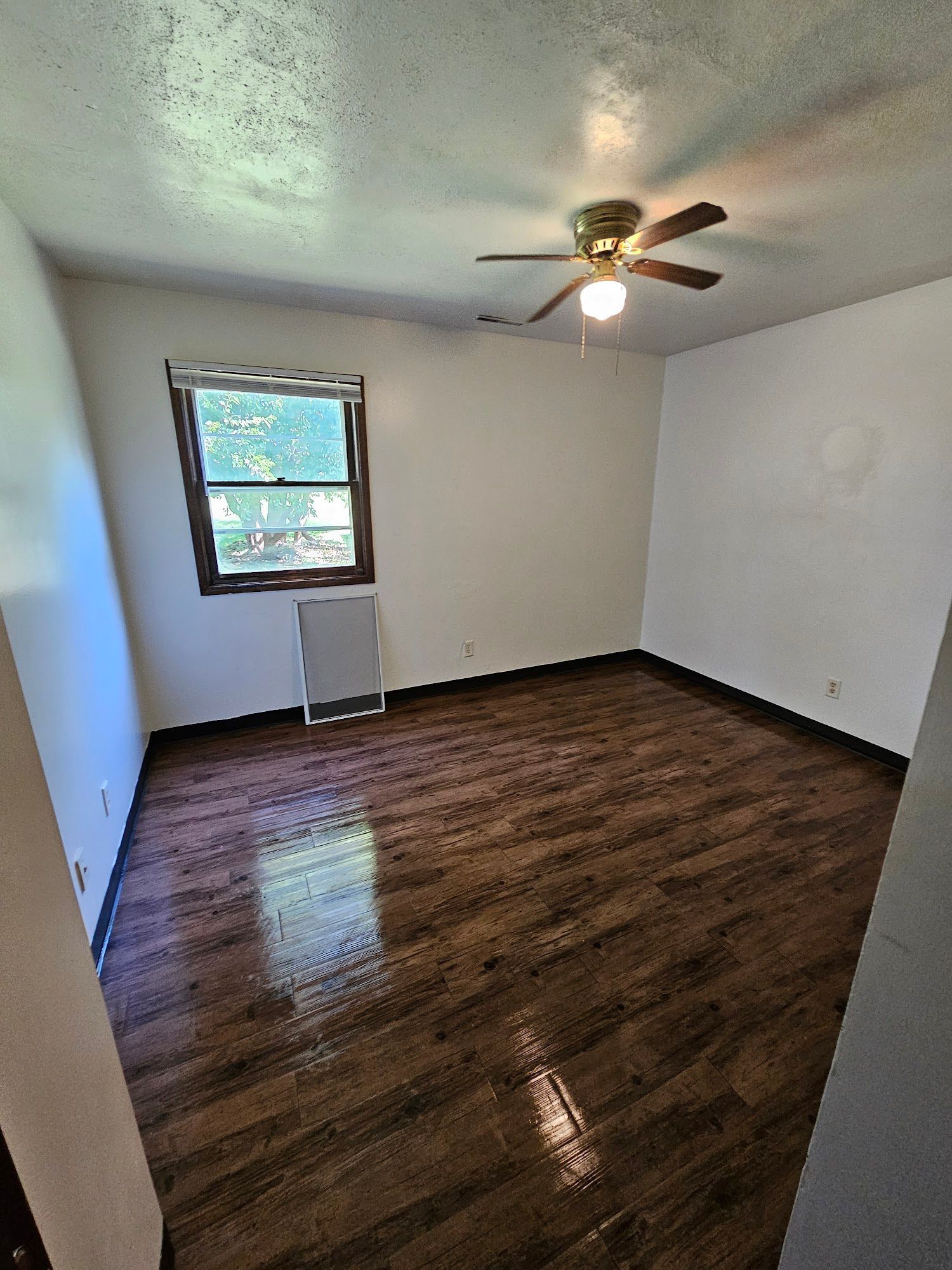 An empty room with a ceiling fan and a window.