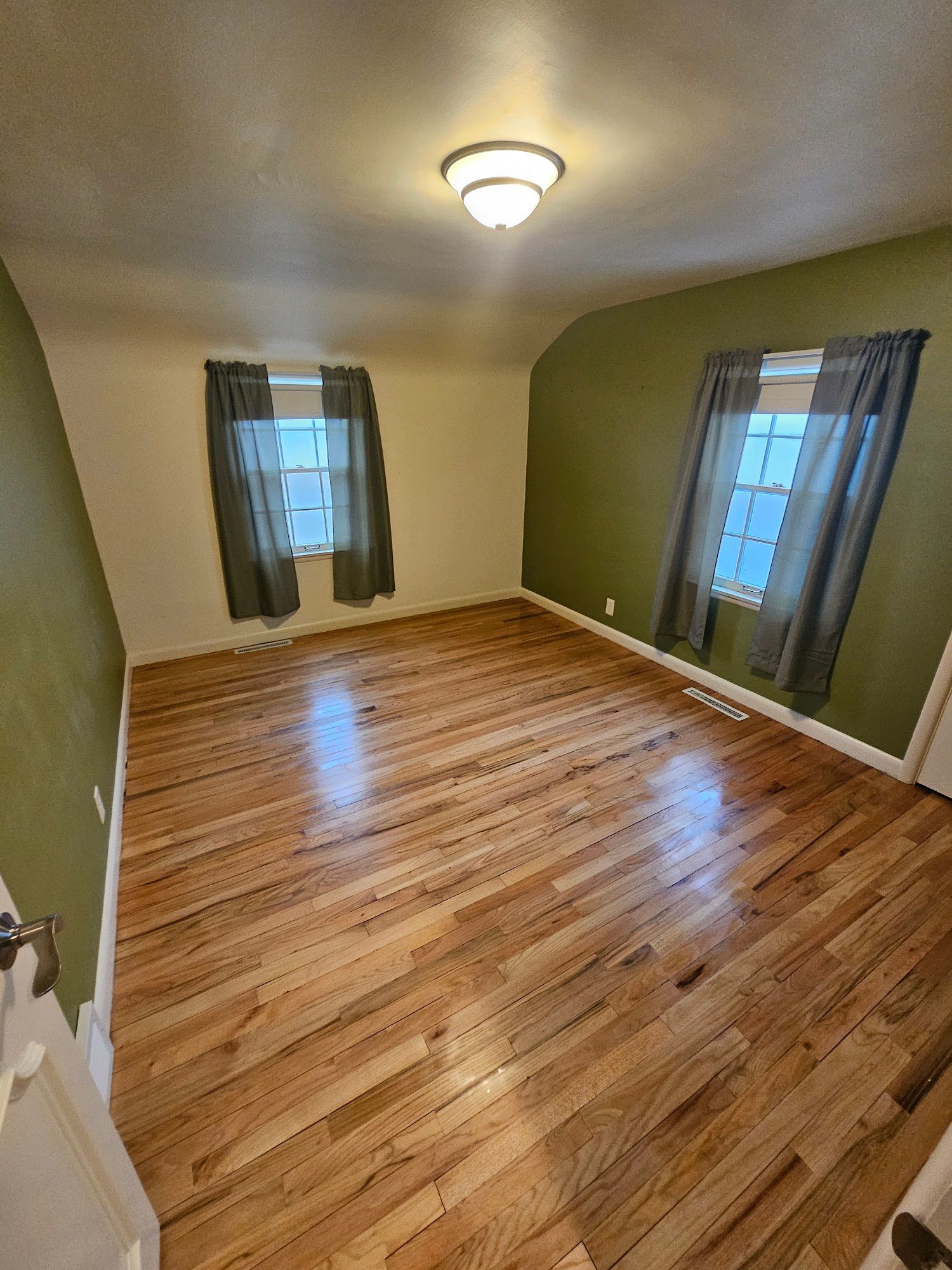 A large empty room with hardwood floors and green walls.