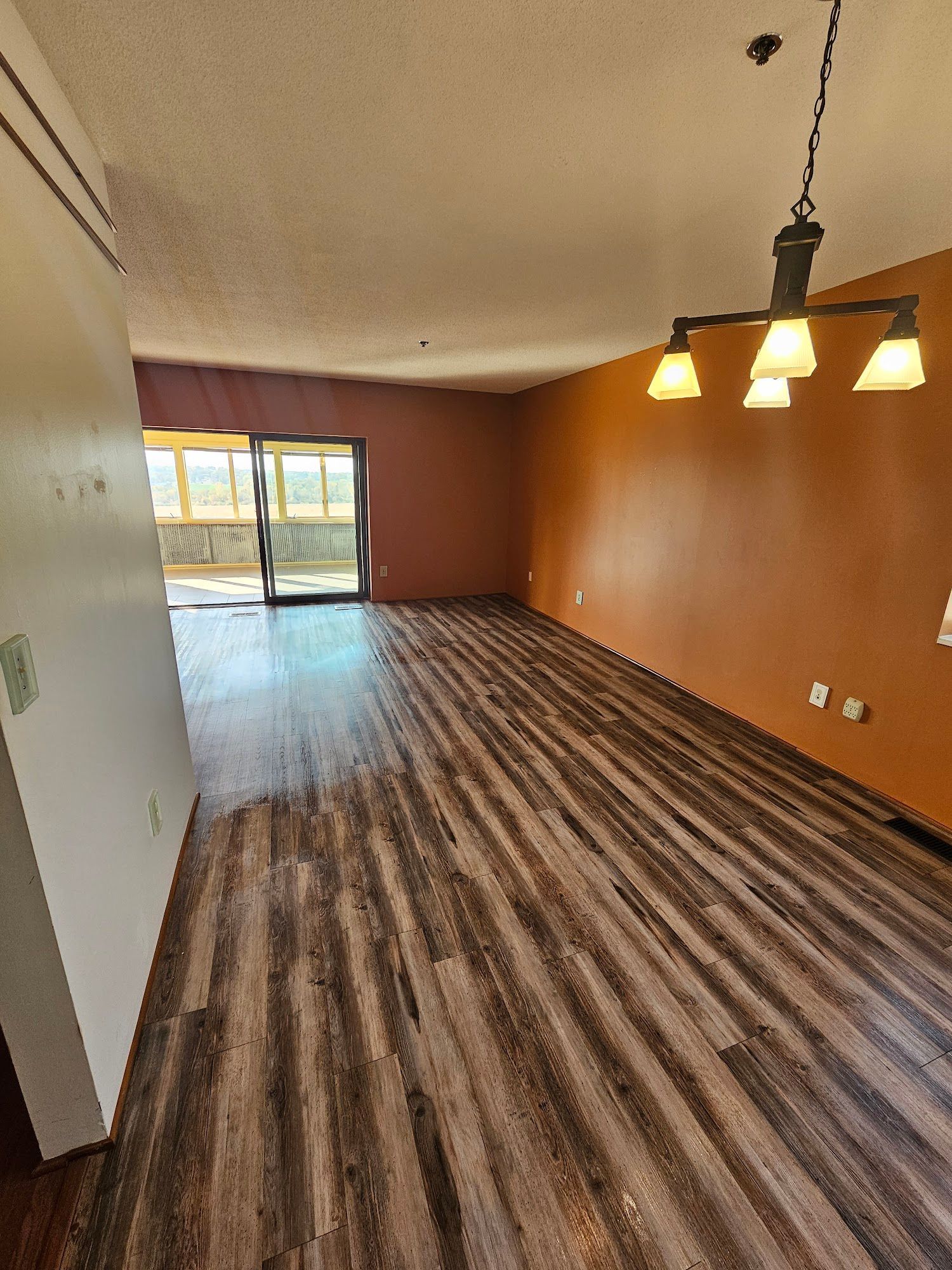 An empty living room with wooden floors and a chandelier hanging from the ceiling.