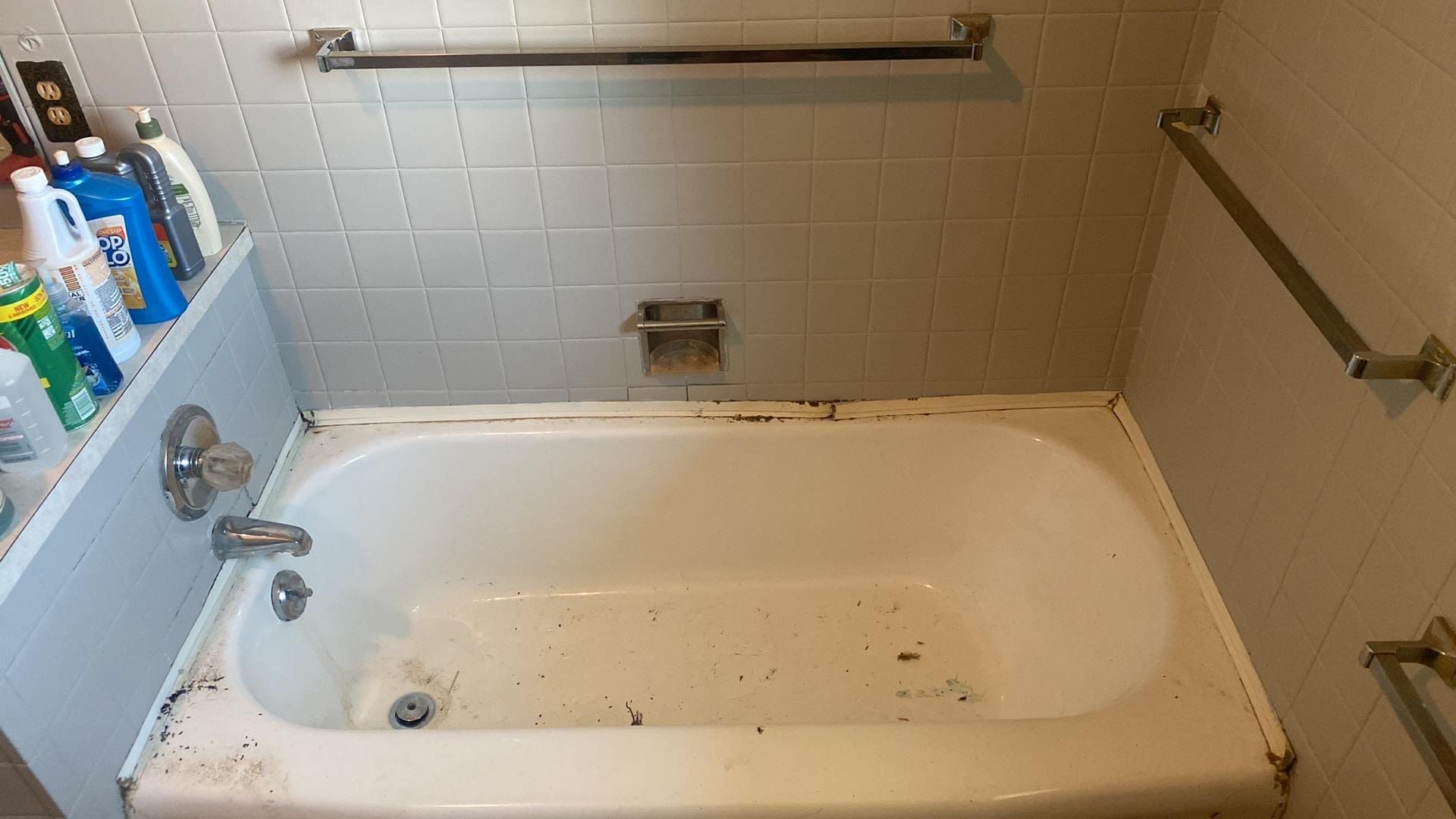 A bathroom with a bathtub and a shelf with cleaning supplies on it.