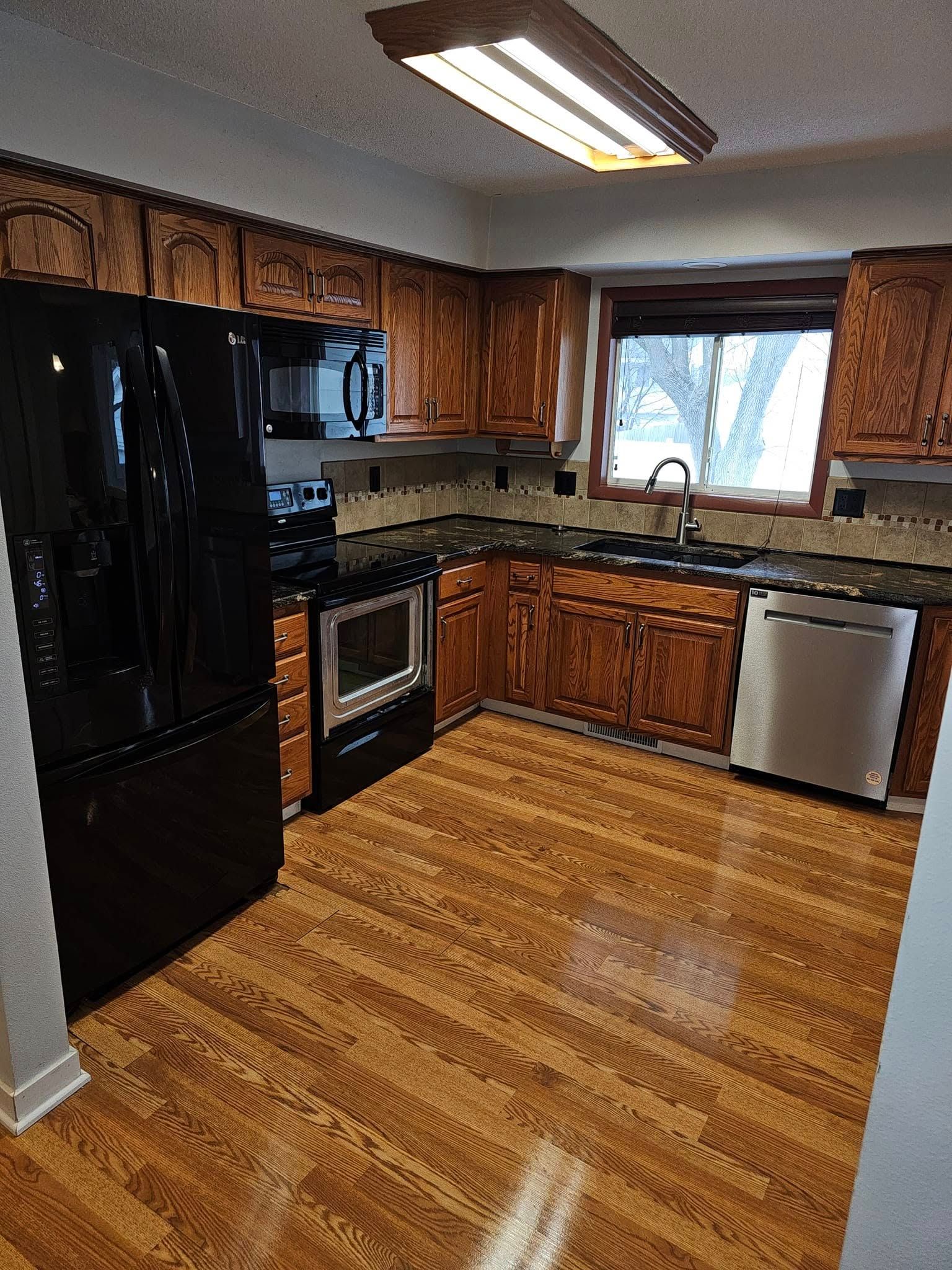 A kitchen with wooden cabinets , stainless steel appliances , and a black refrigerator.