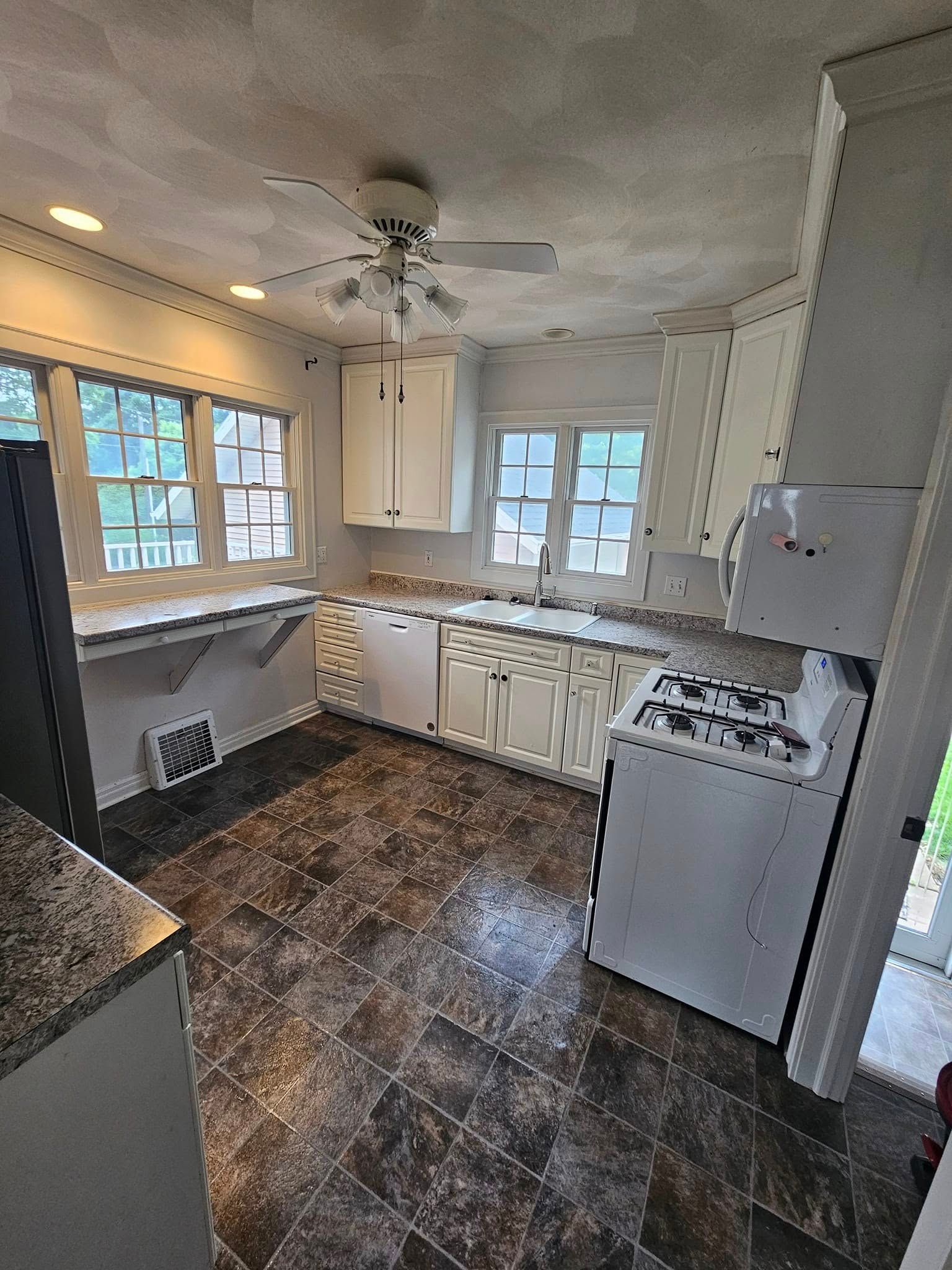 A kitchen with white cabinets , a stove , a refrigerator , and a ceiling fan.